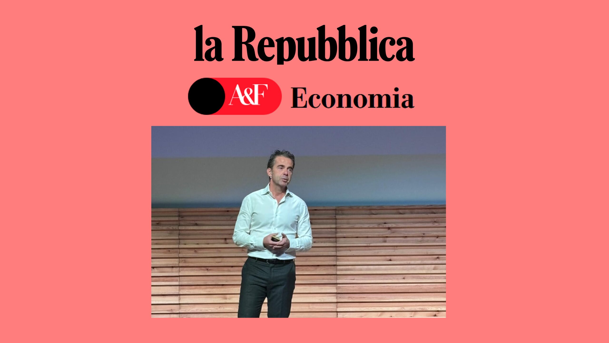 Un uomo in camicia bianca è in piedi sul palco con in mano un dispositivo e sopra di lui i loghi de La Stampa, la Repubblica e l'Economia su uno sfondo rosa salmone. La scena segna un evento che precede il 22 ottobre 2025.