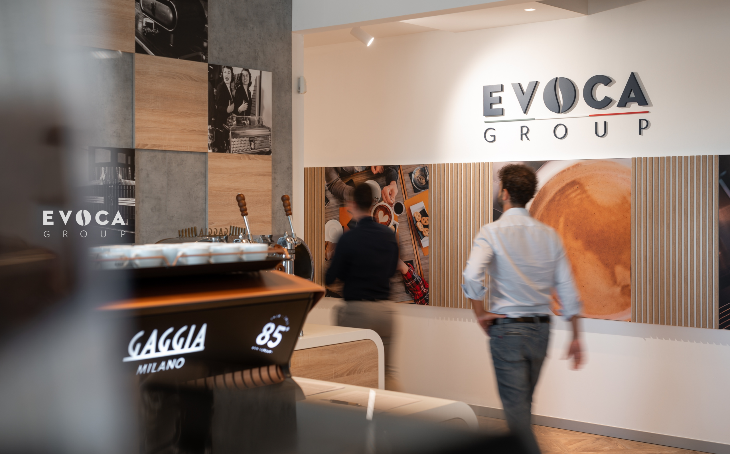 Una donna in giacca e cravatta con una camicetta arancione è in piedi davanti a grafici e diagrammi, con in mano un pennarello. L'immagine presenta elementi grafici in blu, arancione e verde acqua.