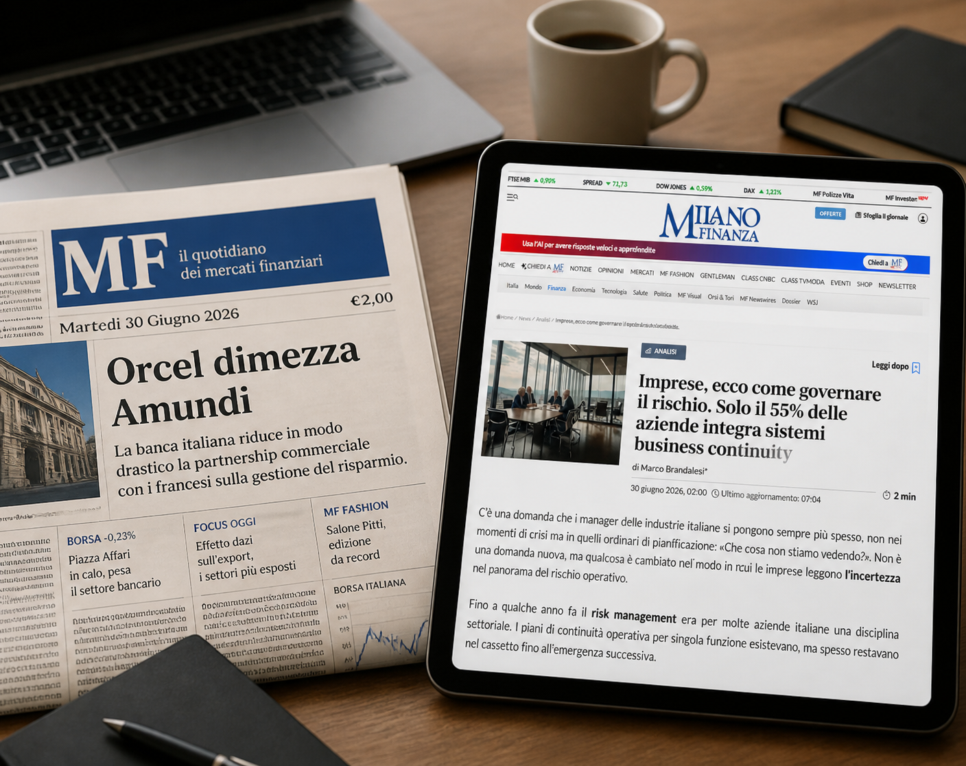 Su una scrivania, su cui sono posati una tazza di caffè, un blocco note, una penna e un paio di occhiali, è aperto un quotidiano finanziario italiano e un tablet su cui è visualizzato un sito di notizie finanziarie con articoli su economia, settore bancario e le ultime novità in materia di tecnologia e innovazione nell'industria digitale.